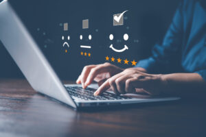 Typing on a laptop with emojis for sad face, neutral face and happy face with the checkmark above the happy face