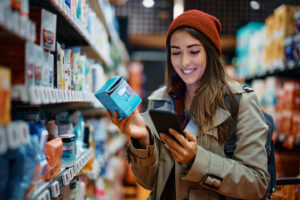 A woman shopping in a store looking at products and checking things out online with her phone.