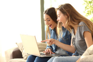 Two women laughing and pointing at a computer screen.