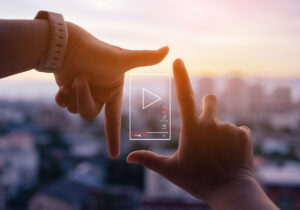 Two hands surrounding a screen with a play button for a video.